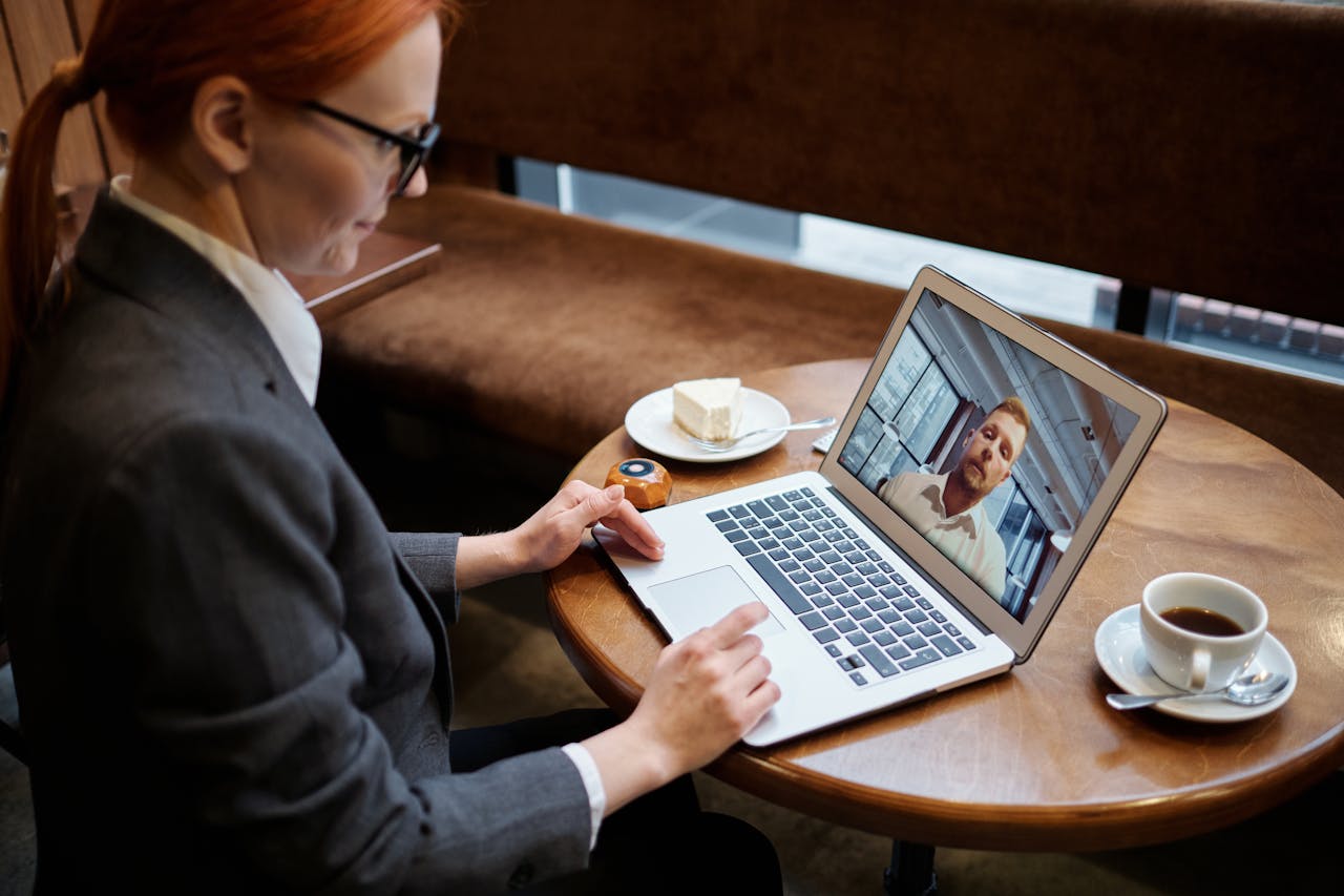 portfolio-02 Business woman engaged in a video call meeting in a cozy cafe setting, using a laptop.